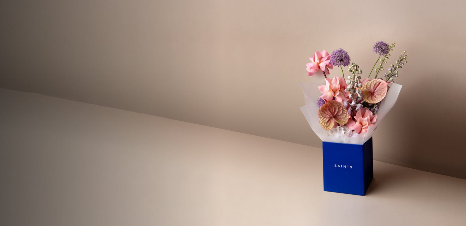 Bouquet of flowers in a blue box with 'SAINTS' branding on a neutral background