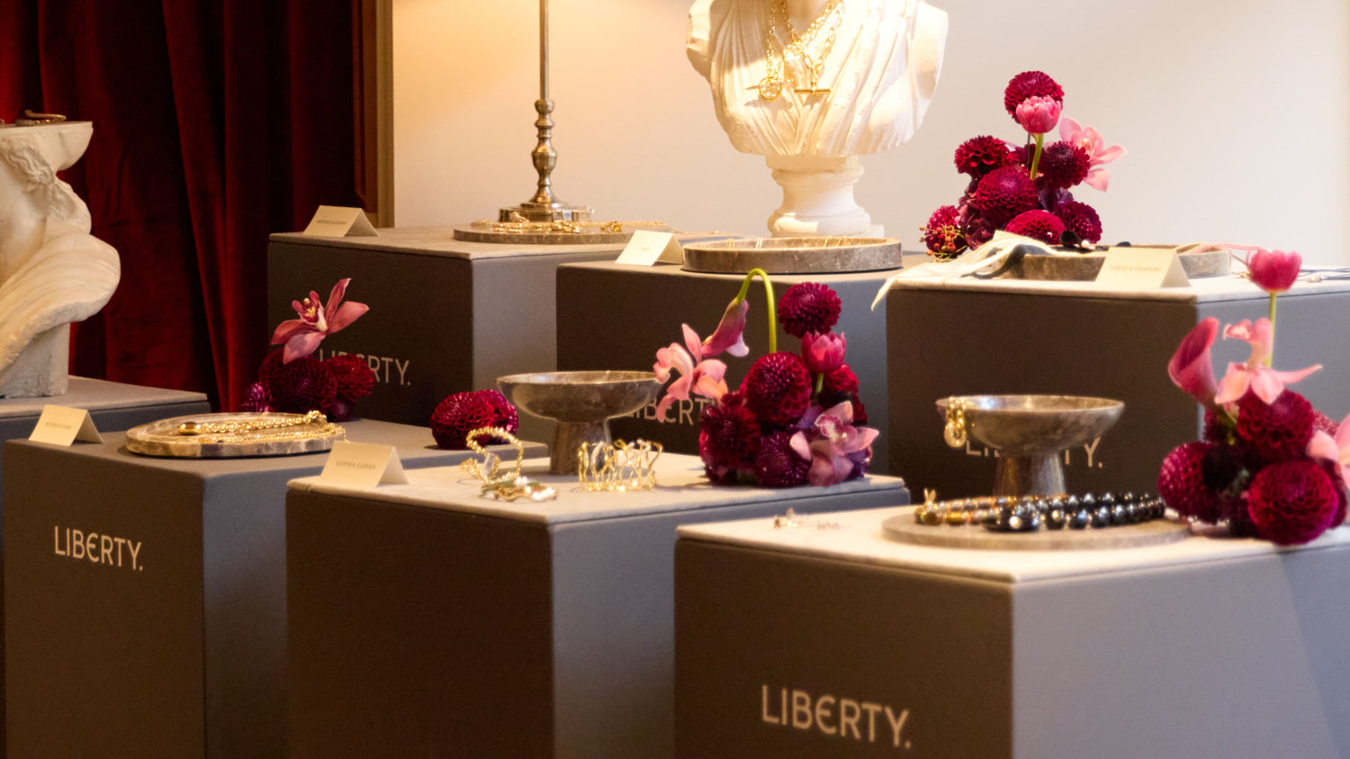 Display case with decorative items including a bust, flowers, and a lamp, branded with 'Liberty'.
