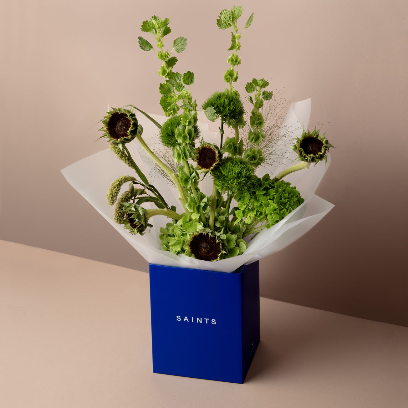 Bouquet of green flowers in a blue box labeled 'SAINTS' on a beige background