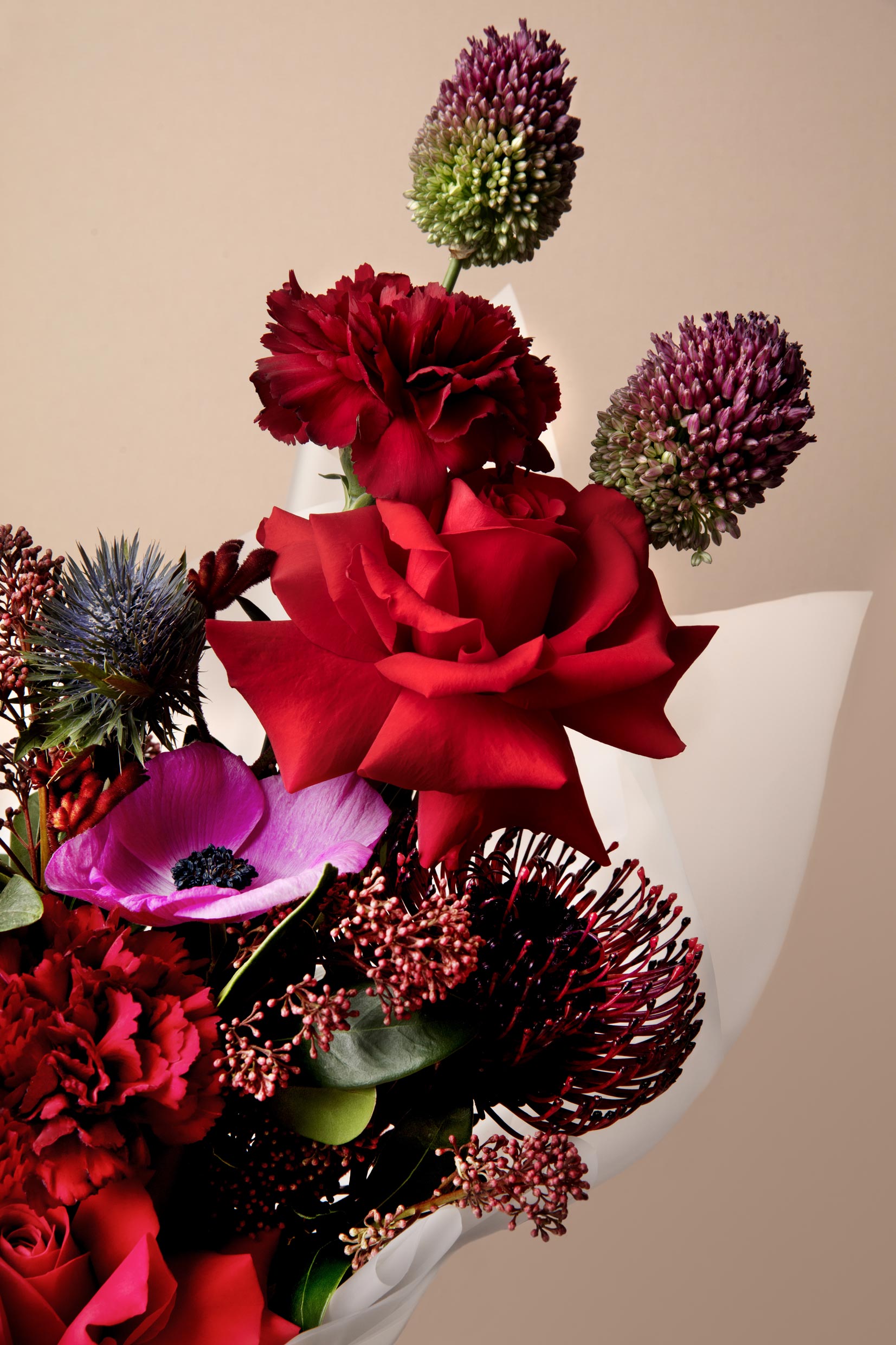 Bouquet of red and pink flowers with greenery on a beige background