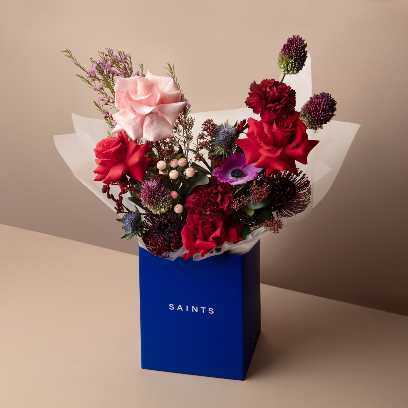 Bouquet of flowers in a blue box with 'SAINTS' branding on a beige background