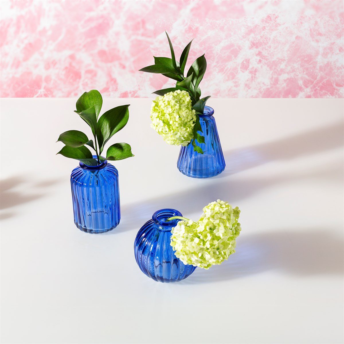 Three blue glass vases with green plants on a light pink background