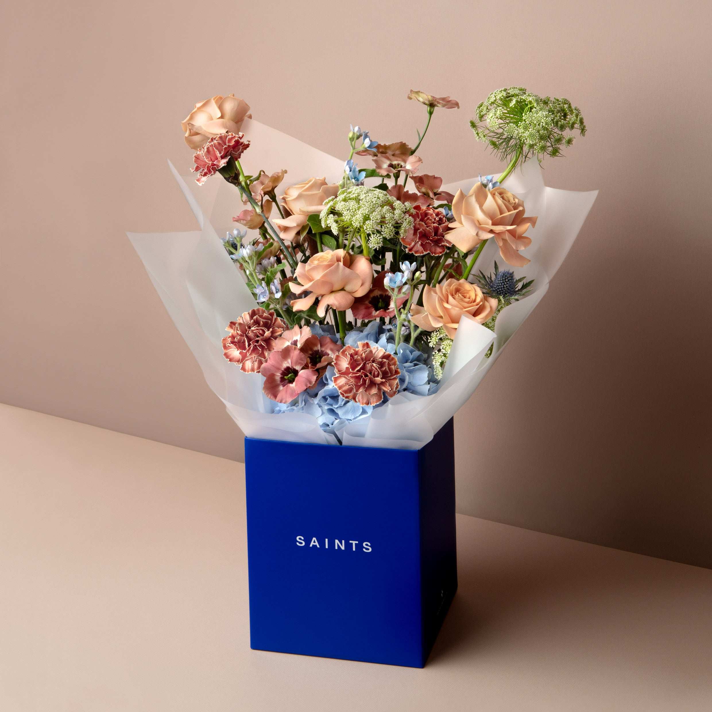 Bouquet of flowers in a blue box labeled 'SAINTS' on a beige background