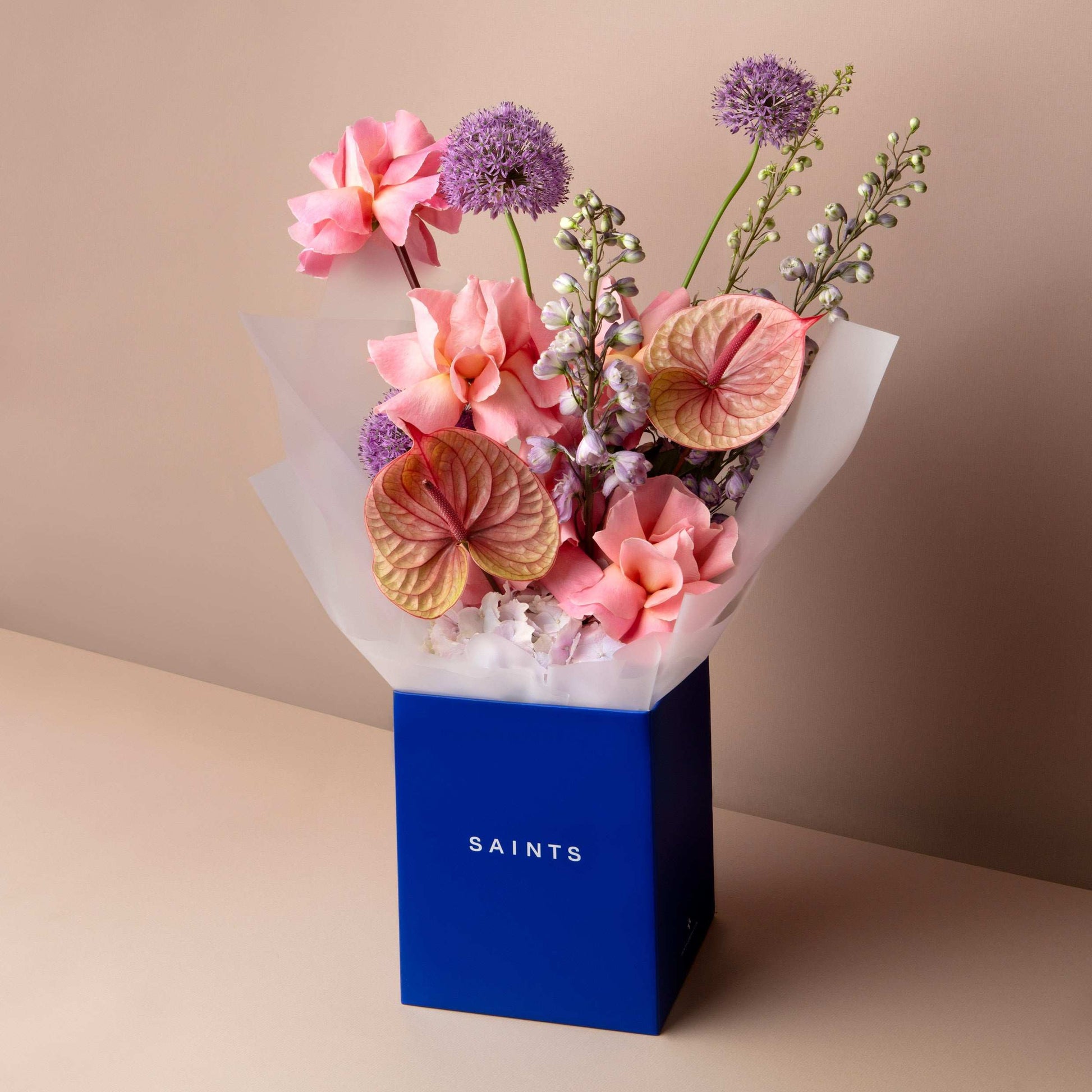 Bouquet of flowers in a blue box labeled 'SAINTS' on a beige background