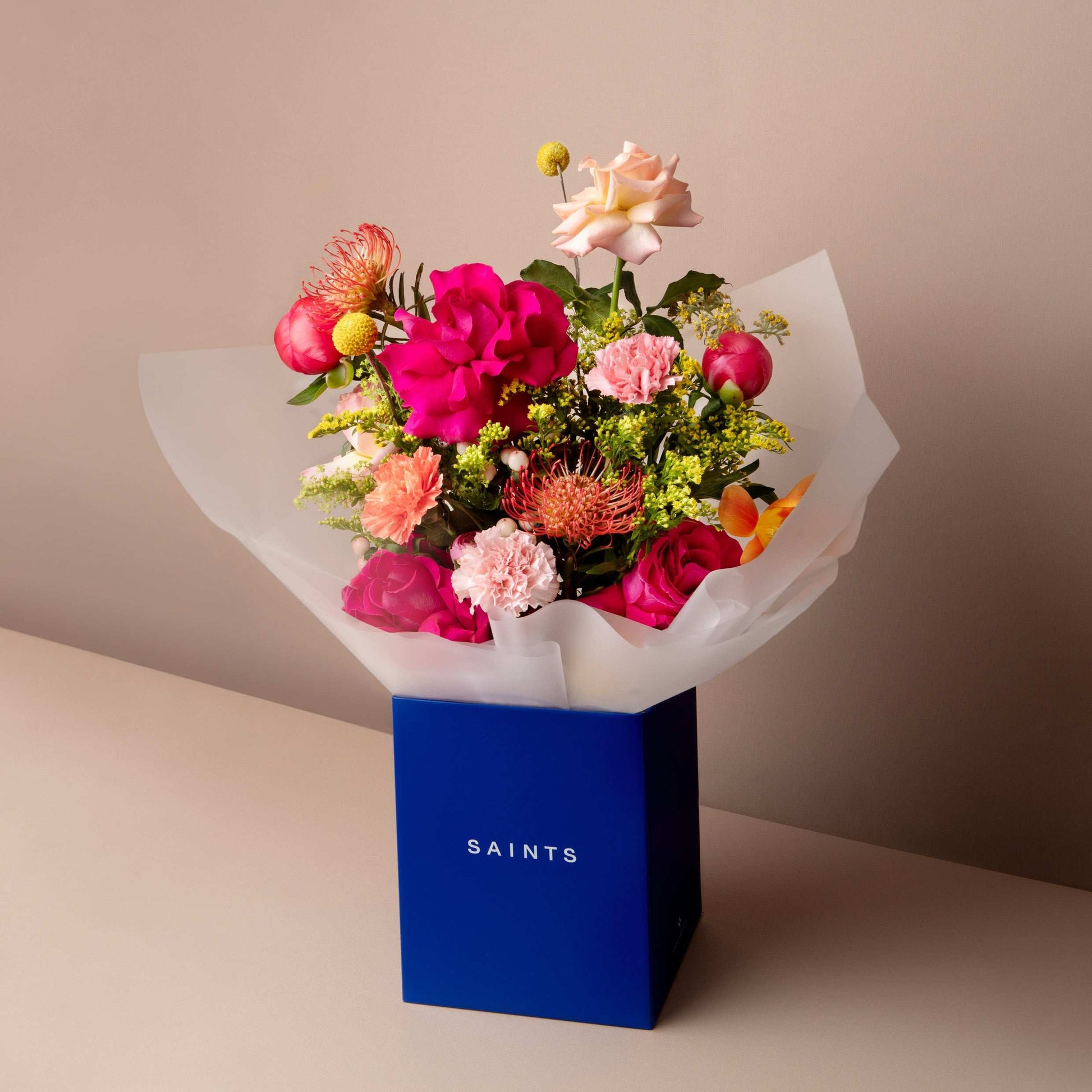Bouquet of flowers in a blue box with 'SAINTS' branding on a beige background