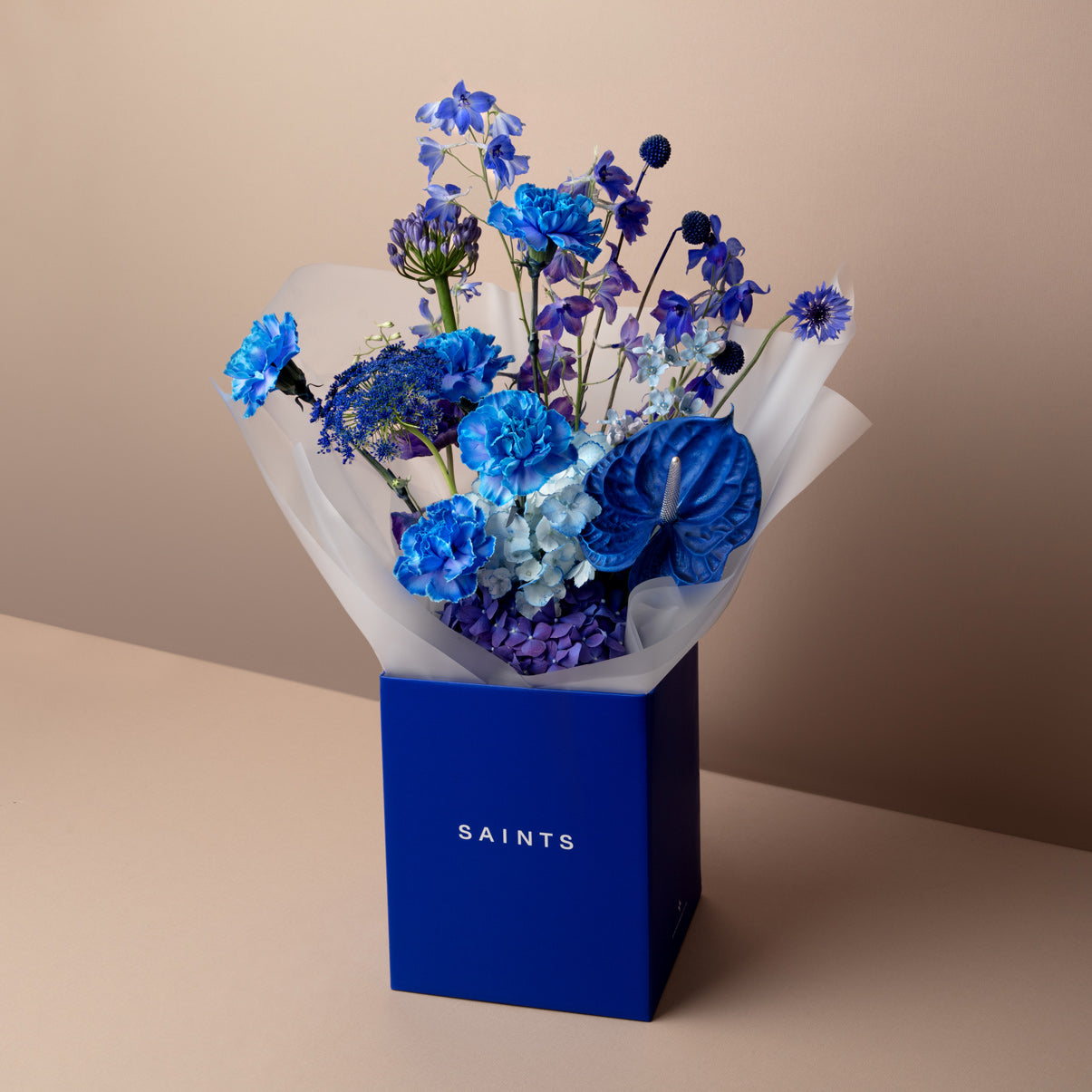 Bouquet of blue flowers in a box labeled 'SAINTS' on a beige background