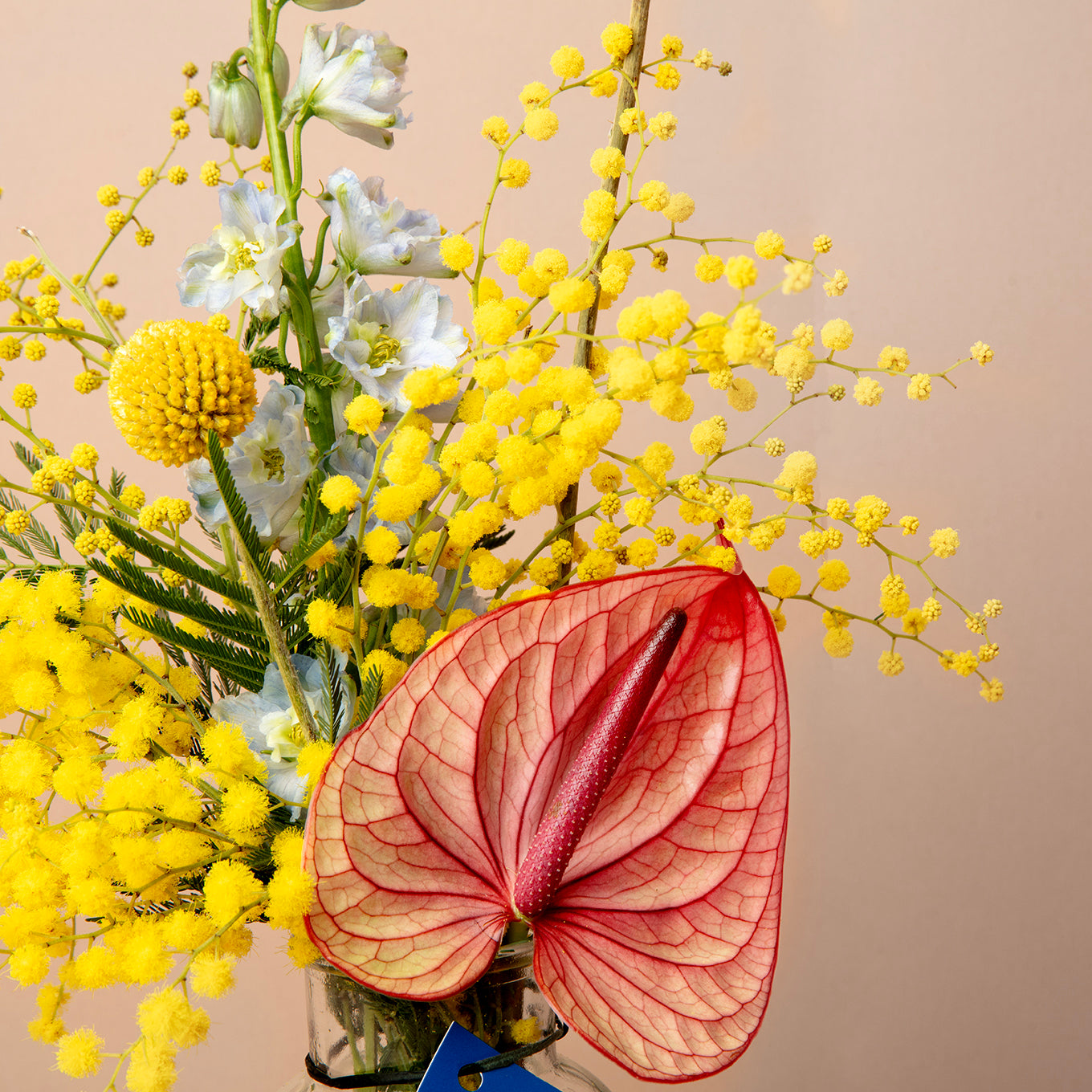 Bouquet of yellow flowers with a large red anthurium leaf on a beige background