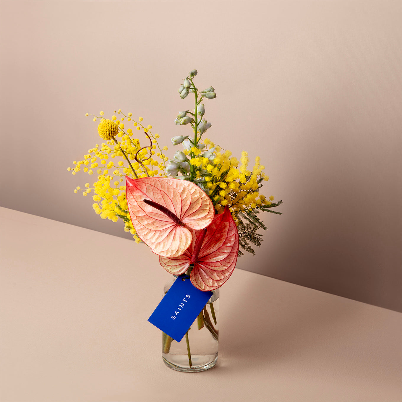 Bouquet of flowers in a clear vase with a blue tag on a beige background