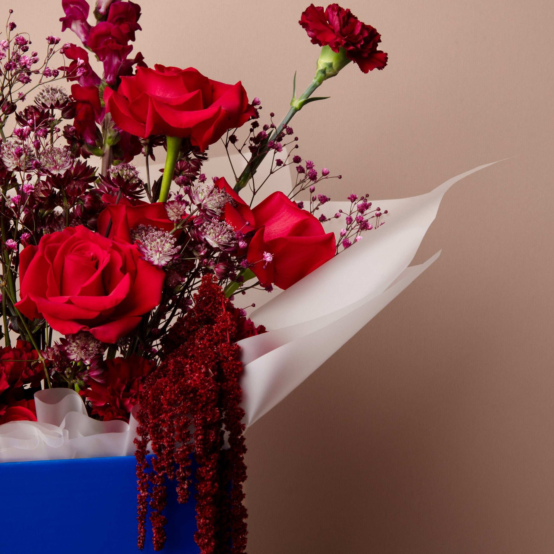 Bouquet of red roses and other flowers with a white ribbon on a beige background