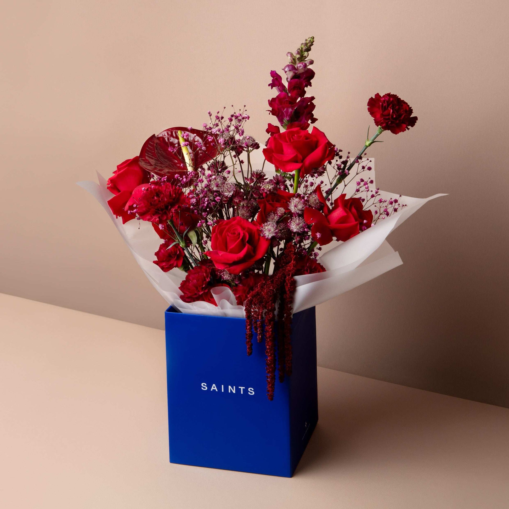 Bouquet of red flowers in a blue box with 'SAINTS' branding on a beige background