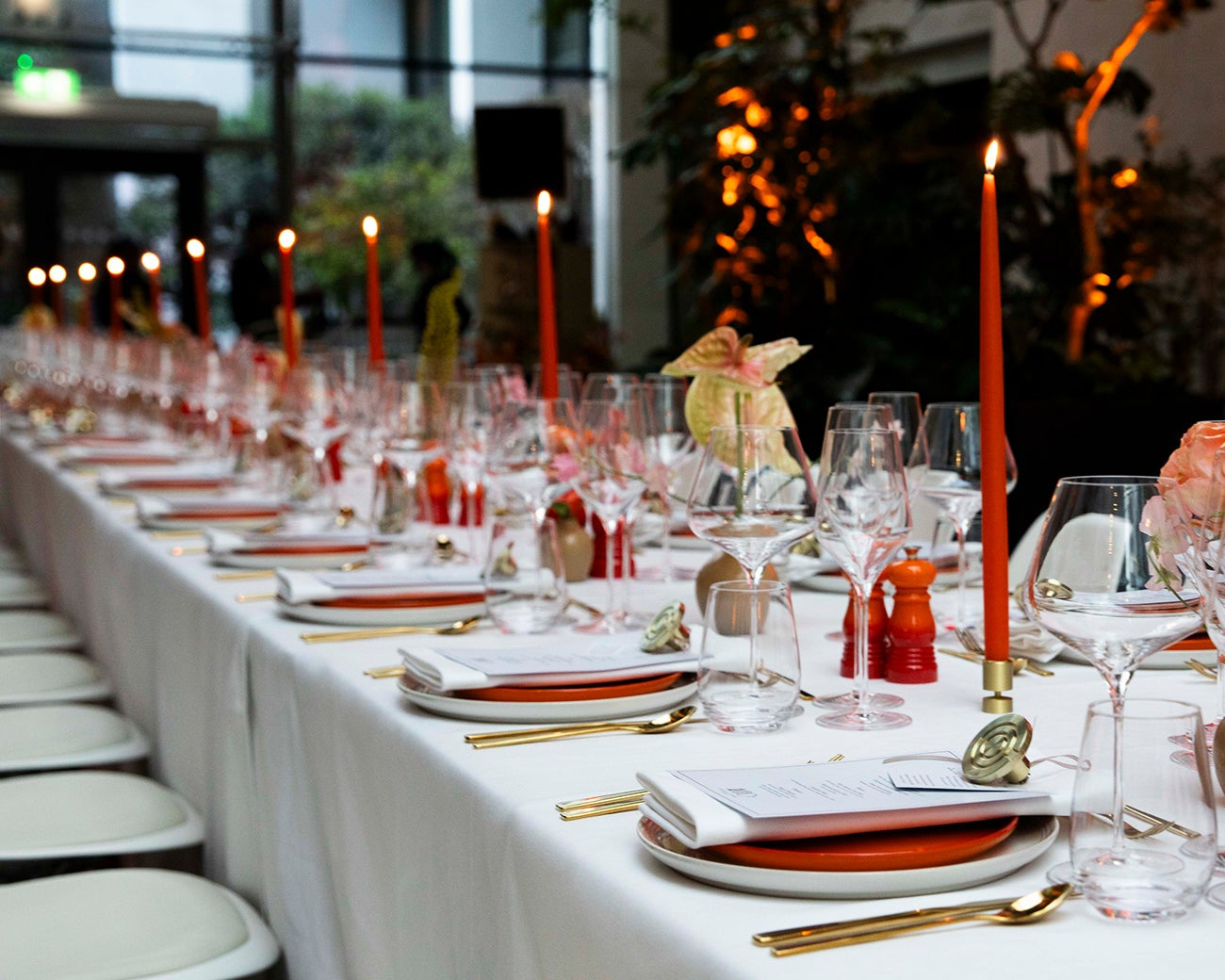 Elegant long table set for a formal event with candles, plates, and glasses.