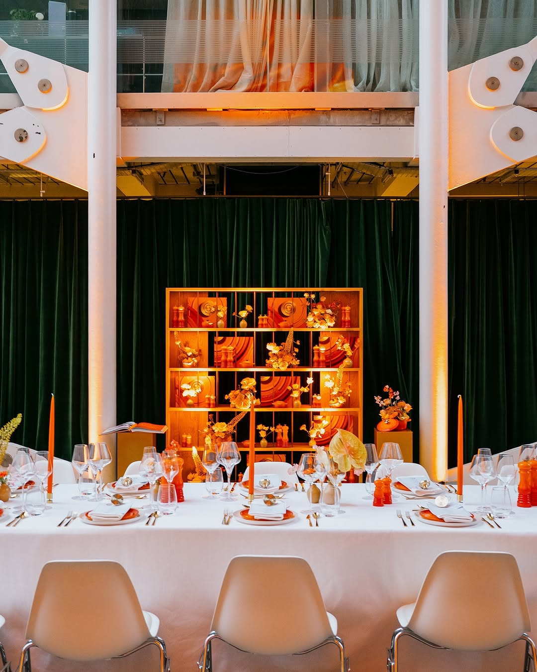 Dining table set for a formal event with white tablecloth, orange candles, and decorative items.