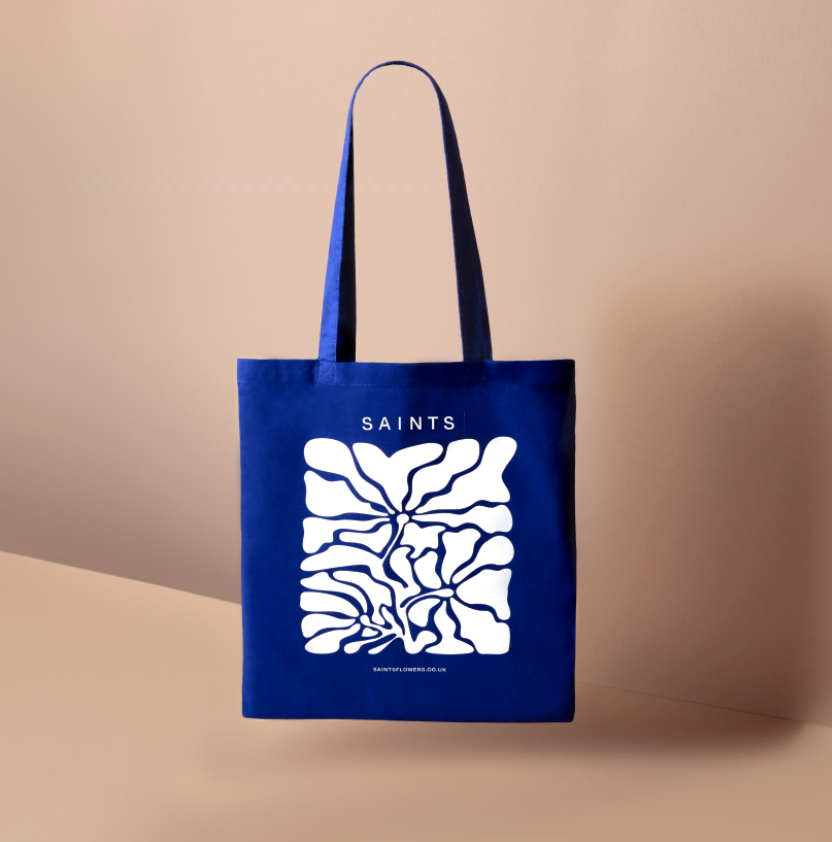 Blue tote bag with white abstract design and 'SAINTS' text on a beige background