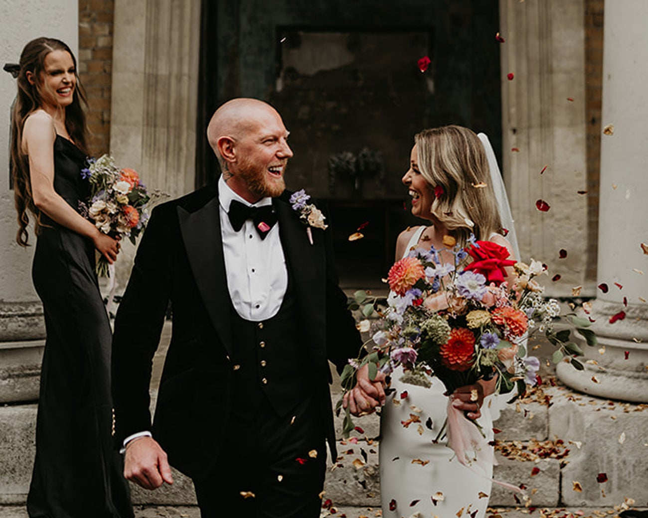 Wedding couple walking down steps with confetti, bride in white dress, groom in black suit, bridesmaid and groomsmen in formal attire.