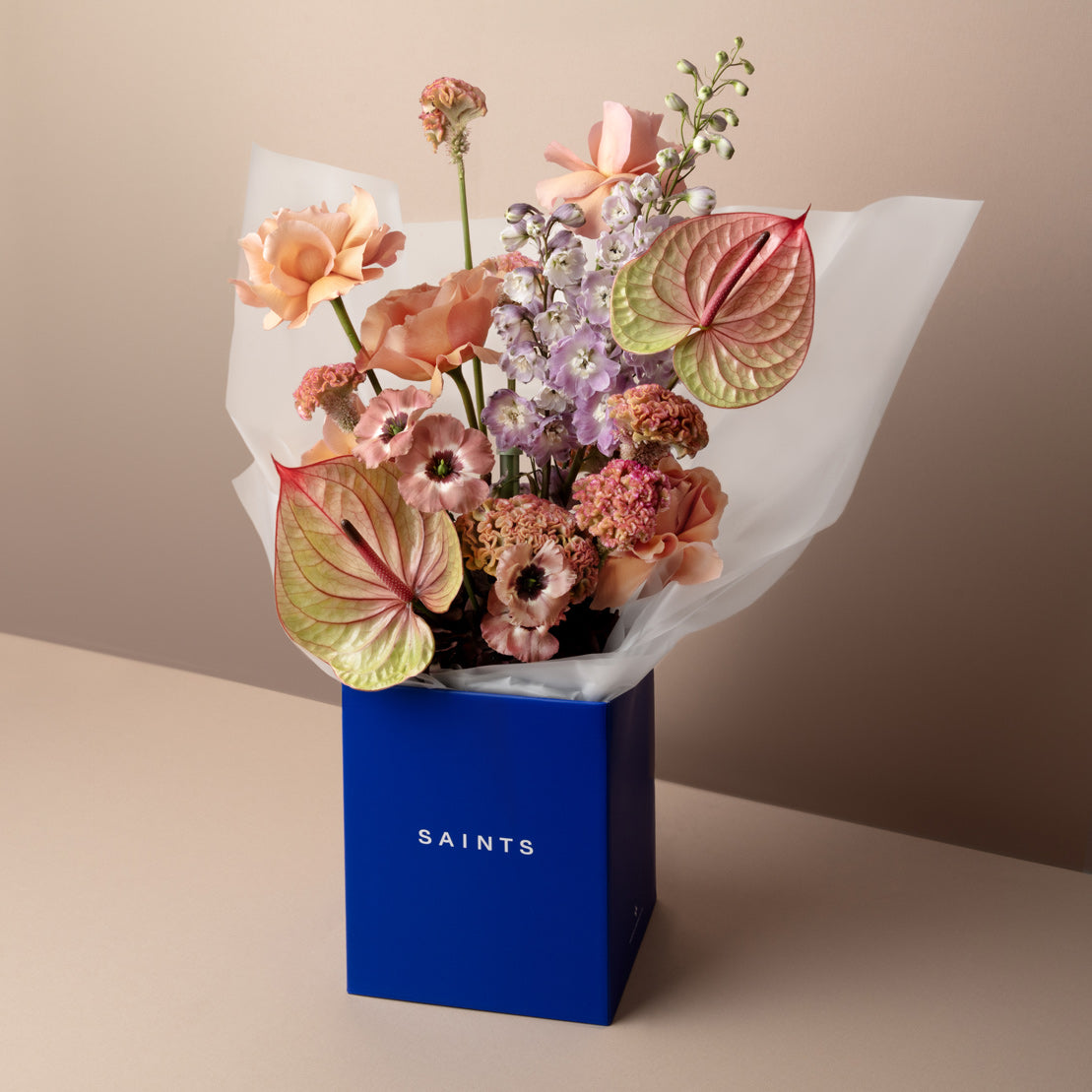 Bouquet of flowers in a blue box with 'SAINTS' branding on a beige background