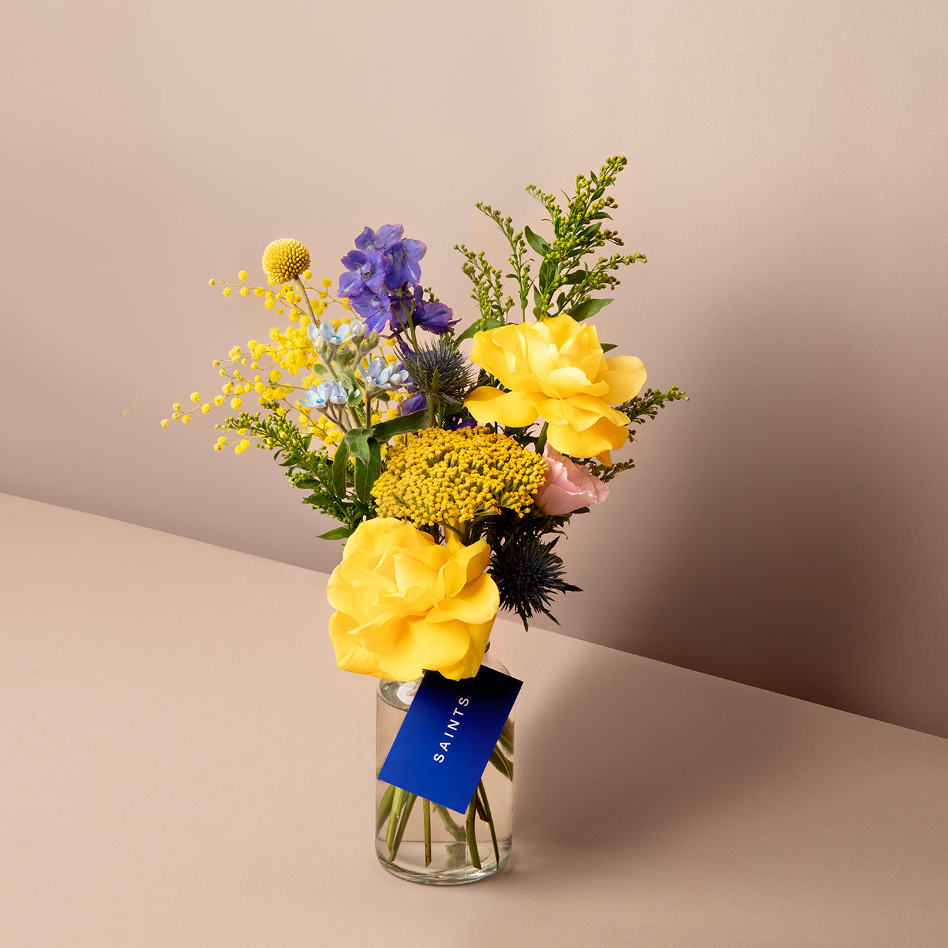 Bouquet of flowers in a clear vase with a visible brand tag on a beige background