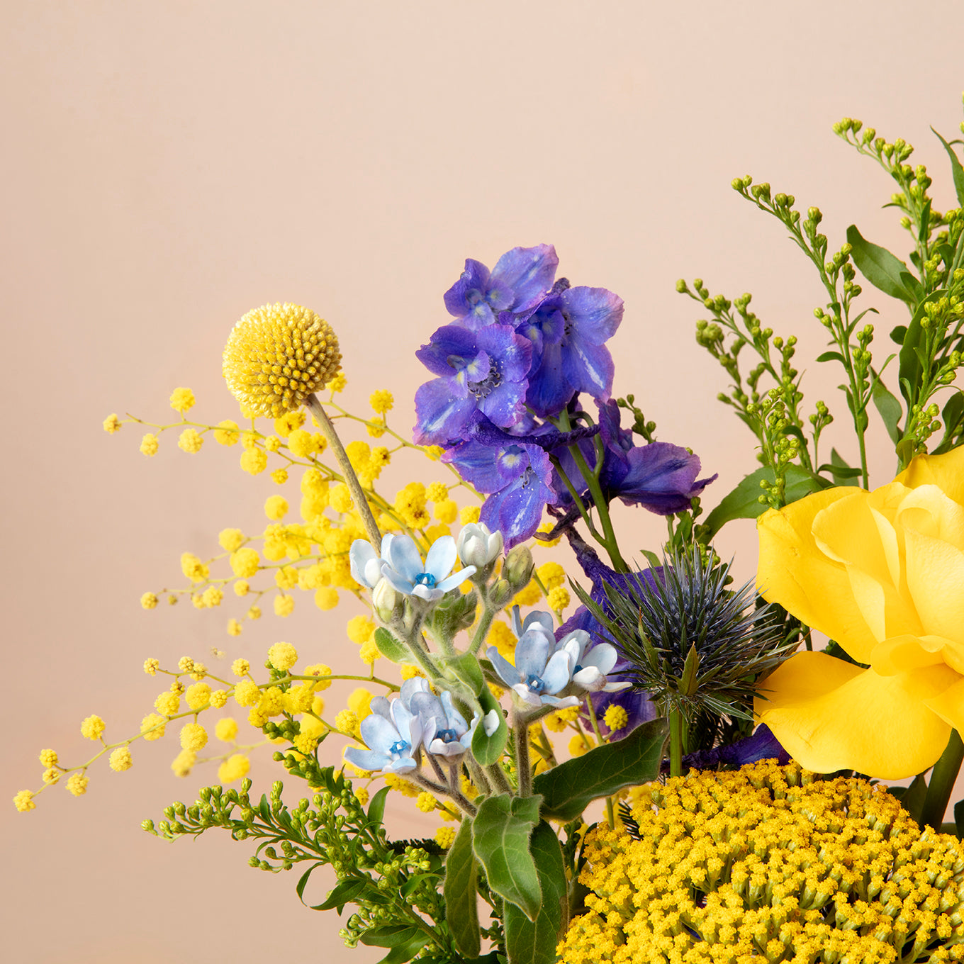 Colorful bouquet of flowers including yellow, blue, and green on a beige background