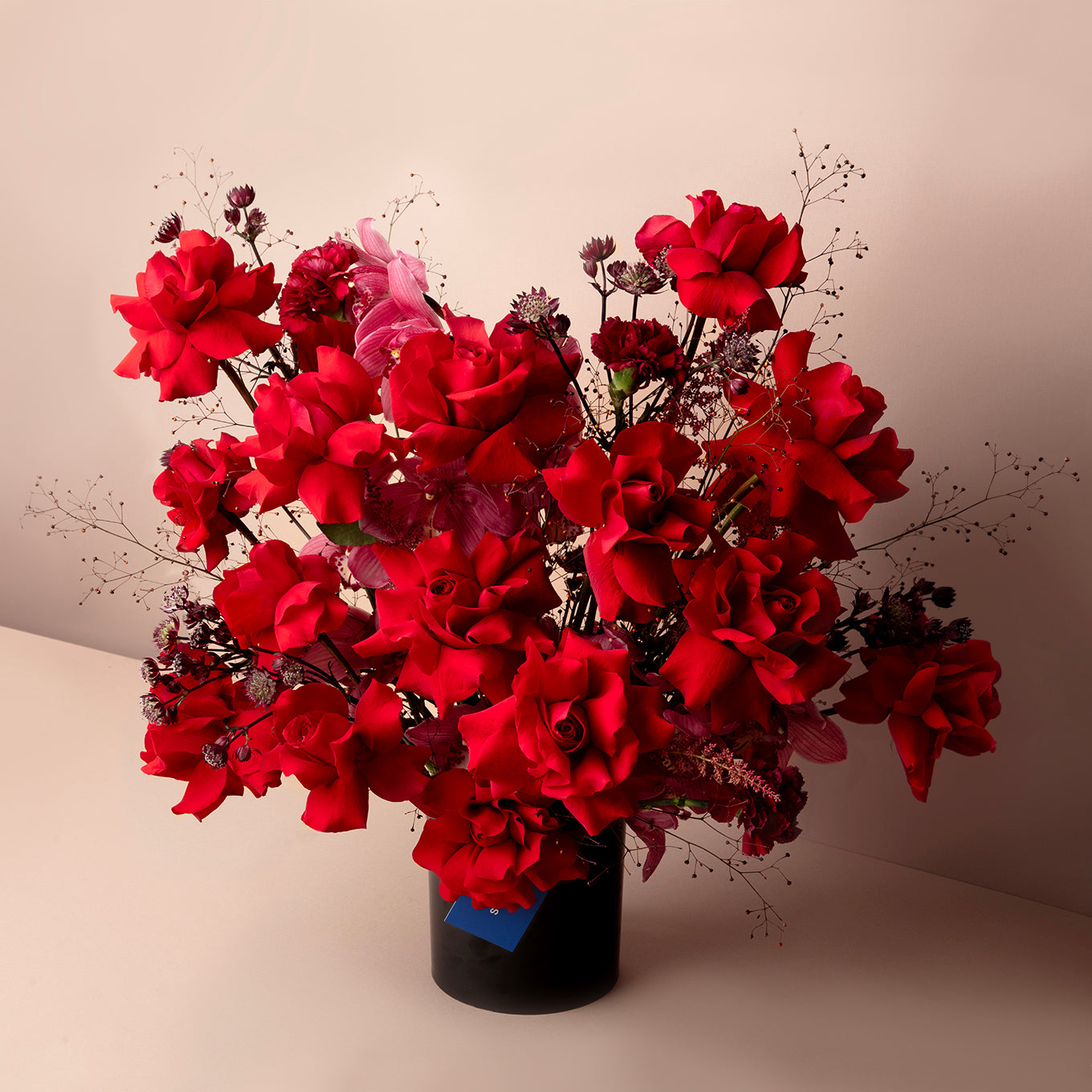 Bouquet of red flowers in a black vase on a beige background