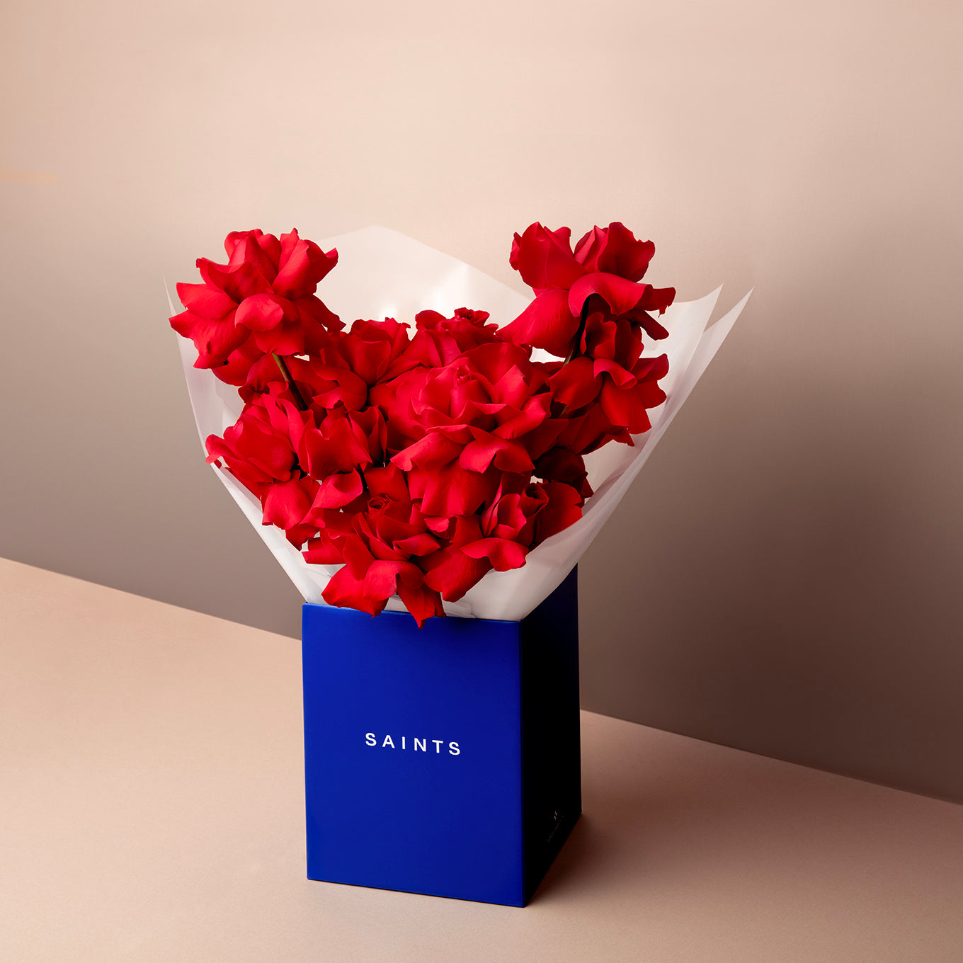 Bouquet of red flowers in a blue box labeled 'SAINTS' on a beige background